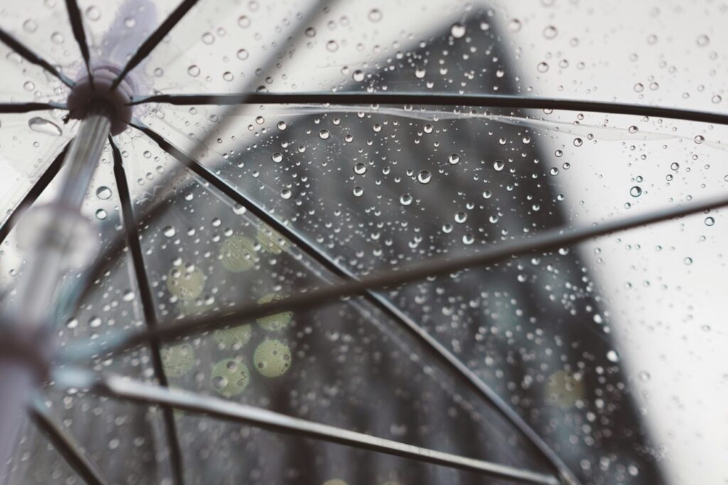 雨粒がついた透明な傘越しに建物が見える、インドネシアの雨季と気候変動を象徴するイメージ画像